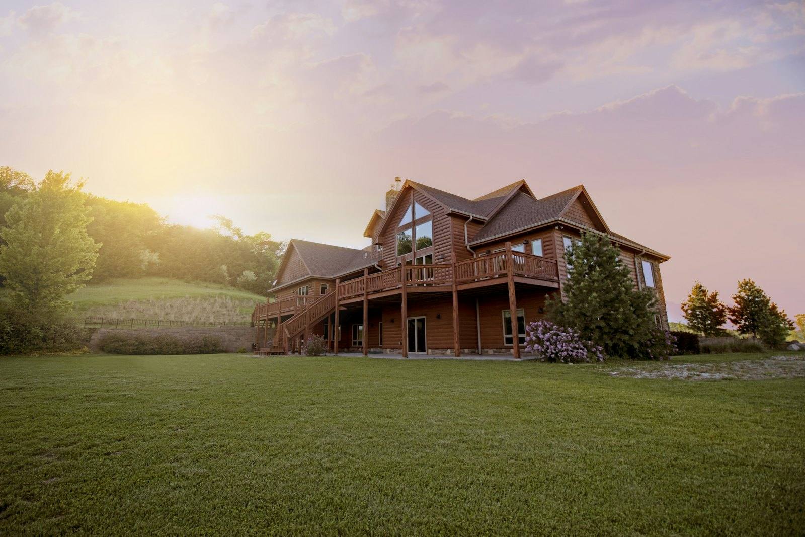 A wood-sided home on a large green lawn at sunset